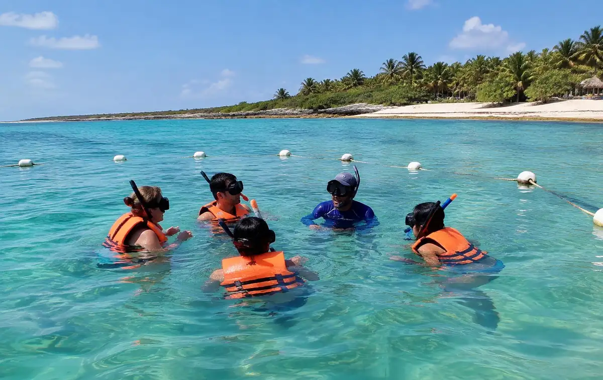 Snorkelers in orange life vests with a guide inside a buoy line at Akumal