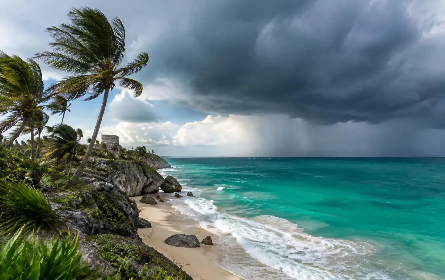 Rain shower over the turquoise sea at Tulum with palm trees bending in wind