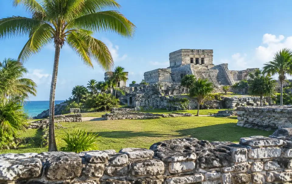 El Castillo temple at the Tulum ruins seen across green lawn and palm trees
